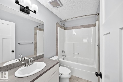 Bathroom featuring a vanity with an oval basin, a rectangular mirror, and a three-light fixture - 1112 176 Street Sw, Edmonton, AB - Indoor Photo Showing Bathroom