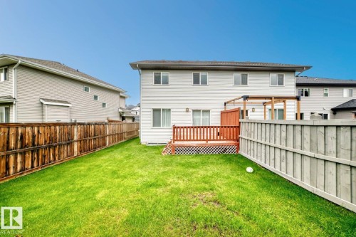 Expansive green space featuring a wooden privacy fence, a raised deck with wood railings, a built-in pergola frame, and sliding glass doors - 1112 176 Street Sw, Edmonton, AB - Outdoor With Deck Patio Veranda With Exterior