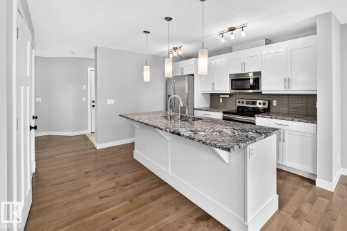 Kitchen featuring a central island with a stone countertop, stainless steel appliances, and white cabinetry - 1112 176 Street Sw, Edmonton, AB - Indoor Photo Showing Kitchen With Upgraded Kitchen