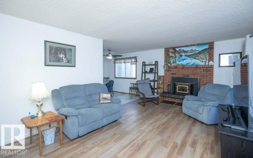 Living area featuring wood-finish flooring, a brick fireplace with a wood stove insert, and white walls - 10729 108A Avenue, Westlock, AB - Indoor Photo Showing Living Room With Fireplace