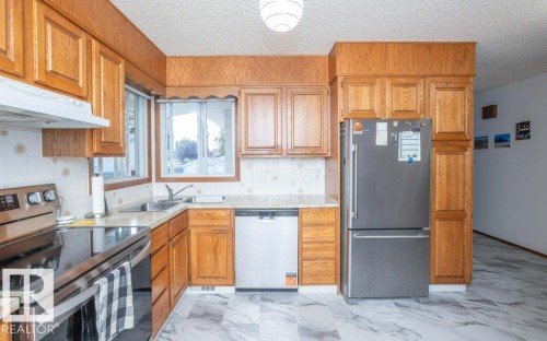 Wood cabinetry and paneling, stainless steel appliances, corner sink with window, tile backsplash, and marble-look flooring - 10729 108A Avenue, Westlock, AB - Indoor Photo Showing Kitchen With Double Sink