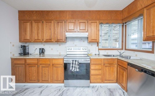 Wood-finish cabinetry paired with light-toned countertops, white tile backsplash, stainless steel electric range, and stainless steel dishwasher - 10729 108A Avenue, Westlock, AB - Indoor Photo Showing Kitchen With Double Sink