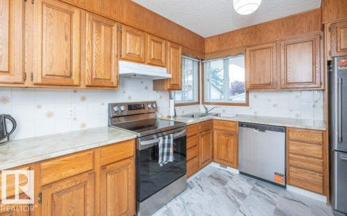 Kitchen with wood cabinetry, stainless steel appliances, patterned backsplash, light-toned countertops, and marbelized flooring - 10729 108A Avenue, Westlock, AB - Indoor Photo Showing Kitchen