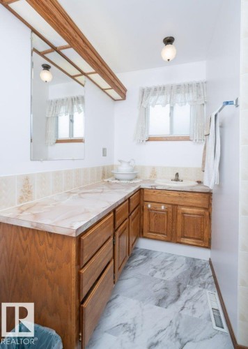 Wood-finish cabinetry with a corner sink, a light-toned countertop, and marble-look flooring - 10729 108A Avenue, Westlock, AB - Indoor