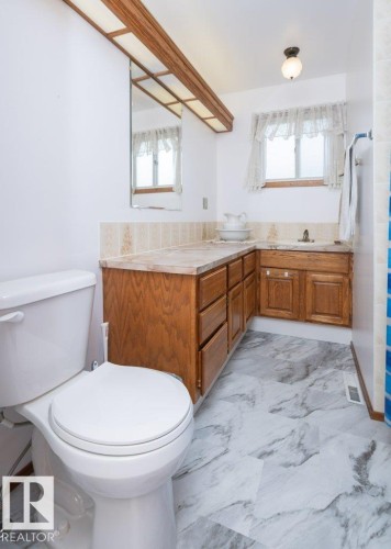 White wall surfaces, wood-finish vanity with countertop, white toilet, and gray marble-look flooring - 10729 108A Avenue, Westlock, AB - Indoor Photo Showing Bathroom