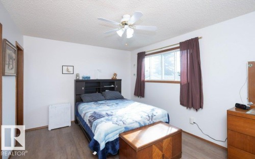 Wood-finish flooring, white painted walls, ceiling fan, and a single window with wood trim - 10729 108A Avenue, Westlock, AB - Indoor Photo Showing Bedroom