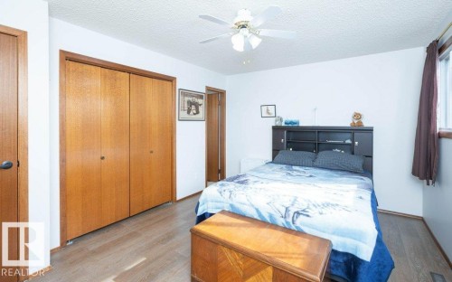 Wood-finish flooring, built-in closet with bi-fold doors, white ceiling fan, built-in headboard with integrated shelving - 10729 108A Avenue, Westlock, AB - Indoor Photo Showing Bedroom