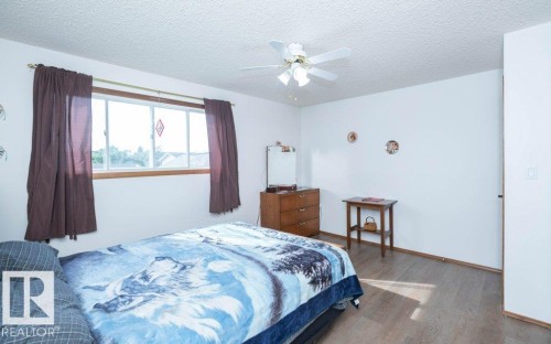 Bright interior with wood-finish flooring, a ceiling fan with integrated lighting, and a wide window with wood trim - 10729 108A Avenue, Westlock, AB - Indoor Photo Showing Bedroom