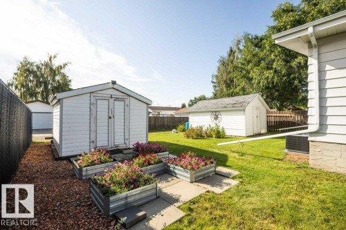 Expansive yard space featuring two storage sheds, manicured lawn, and raised garden beds - 10729 108A Avenue, Westlock, AB - Outdoor With Exterior