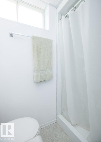 White shower enclosure with a white shower curtain, white toilet, and light-toned flooring - 10729 108A Avenue, Westlock, AB - Indoor Photo Showing Bathroom