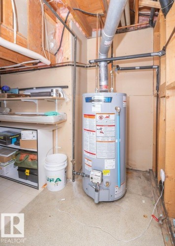 Water heater installation with exposed wood ceiling beams, exposed insulation, and utility shelving - 10729 108A Avenue, Westlock, AB - Indoor Photo Showing Basement