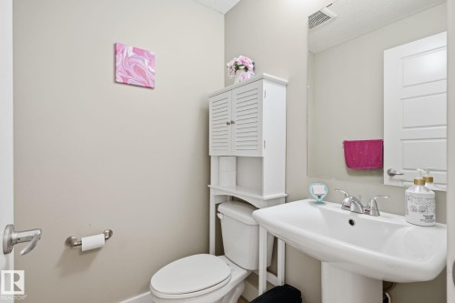 Pedestal sink with chrome faucet, toilet with overhead storage cabinet, and large wall-mounted mirror - 944 Morris Way, Leduc, AB - Indoor Photo Showing Bathroom