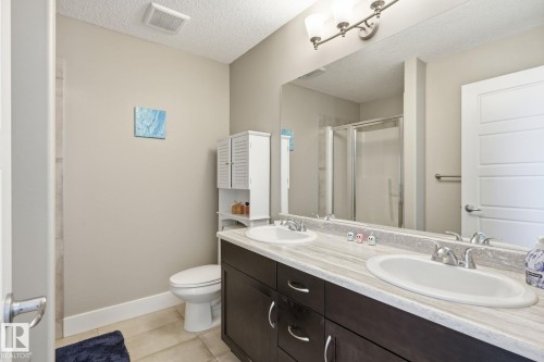 Dual vanity with integrated sinks, dark wood-finish cabinetry, and a full-width mirror - 944 Morris Way, Leduc, AB - Indoor Photo Showing Bathroom