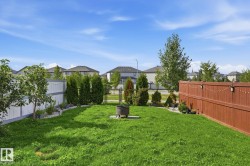 Expansive backyard featuring a lush lawn, privacy fencing, mature trees, and a dedicated fire pit area - 