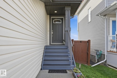 Front entry featuring a dark gray door with an arched glass insert, covered porch, and white horizontal siding - 944 Morris Way, Leduc, AB - Outdoor With Exterior