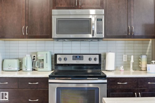 Stainless steel microwave and electric range, dark wood-finish cabinetry, light-colored countertop, and a tiled backsplash - 944 Morris Way, Leduc, AB - Indoor Photo Showing Kitchen With Upgraded Kitchen