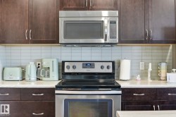 Stainless steel microwave and electric range, dark wood-finish cabinetry, light-colored countertop, and a tiled backsplash - 