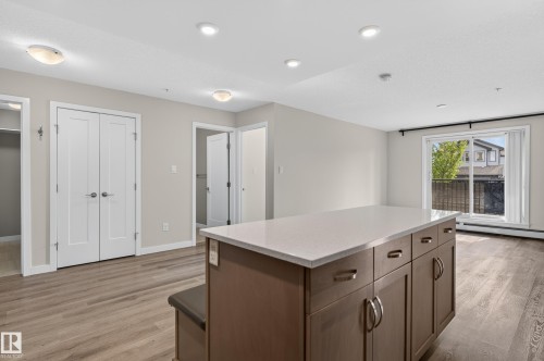 Central kitchen island with a light-toned countertop, wood-finish flooring, sliding glass patio door, and recessed lighting - #131 5504 Schonsee Dr Nw, Edmonton, AB - Indoor