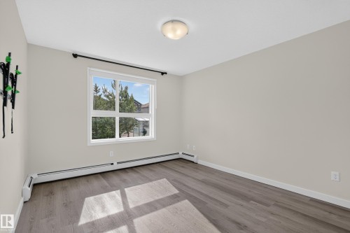 Neutral tone walls, wood-finish flooring, and a large window with white trim - #131 5504 Schonsee Dr Nw, Edmonton, AB - Indoor Photo Showing Other Room