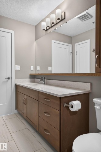 Wood-finish vanity with ample storage, integrated sink, and light-toned countertop - #131 5504 Schonsee Dr Nw, Edmonton, AB - Indoor Photo Showing Bathroom