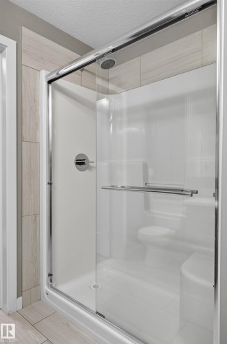 Enclosed shower with sliding glass doors, built-in seating, chrome fixtures, and tiled surround - #131 5504 Schonsee Dr Nw, Edmonton, AB - Indoor Photo Showing Bathroom