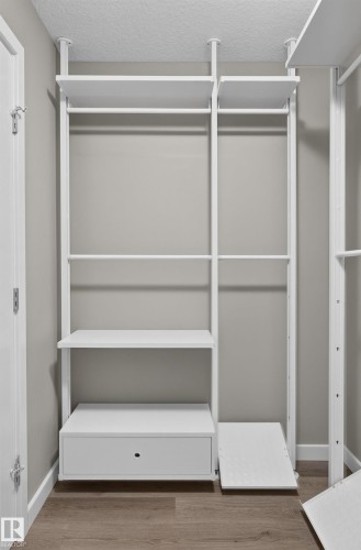 Integrated white closet system featuring multiple shelves, hanging rods, and a drawer - #131 5504 Schonsee Dr Nw, Edmonton, AB - Indoor With Storage