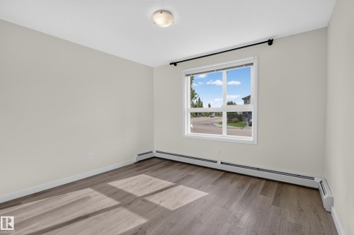 Wood-finish flooring, white walls, and a large window with white framing - #131 5504 Schonsee Dr Nw, Edmonton, AB - Indoor Photo Showing Other Room