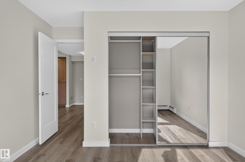 Built-in closet with shelving and mirrored sliding doors, wood-finish flooring, and white interior doors - #131 5504 Schonsee Dr Nw, Edmonton, AB - Indoor Photo Showing Other Room