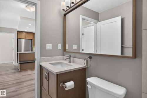 Bathroom featuring a vanity with an integrated sink, a large framed mirror, and a toilet - #131 5504 Schonsee Dr Nw, Edmonton, AB - Indoor Photo Showing Bathroom
