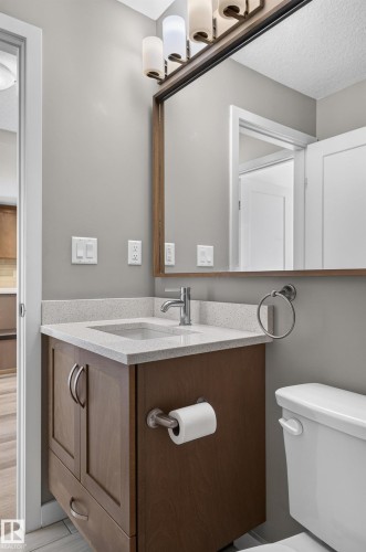 Bathroom vanity featuring a light-toned countertop, integrated sink, and wood-finish cabinetry - #131 5504 Schonsee Dr Nw, Edmonton, AB - Indoor Photo Showing Bathroom