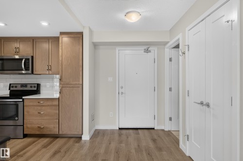 Wood-finish flooring, white subway tile backsplash, stainless steel appliances, recessed ceiling lights, and flat-panel cabinetry - #131 5504 Schonsee Dr Nw, Edmonton, AB - Indoor Photo Showing Kitchen