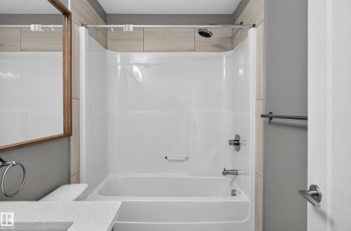 Built-in bathtub with a white surround and chrome fixtures, featuring a rainfall showerhead - #131 5504 Schonsee Dr Nw, Edmonton, AB - Indoor Photo Showing Bathroom