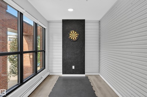 Full-height windows with black framing, wood-finish flooring, recessed ceiling lighting, and textured wall paneling - #131 5504 Schonsee Dr Nw, Edmonton, AB - Indoor Photo Showing Other Room