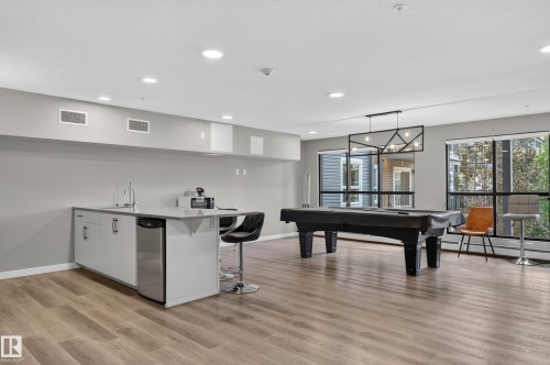 Expansive common area featuring wood-finish flooring, a built-in wet bar with stainless steel appliances, large windows, and recessed lighting - #131 5504 Schonsee Dr Nw, Edmonton, AB - Indoor Photo Showing Other Room