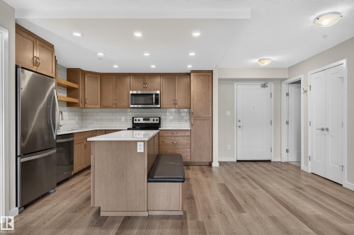 Modern kitchen featuring wood-finish cabinetry, stainless steel appliances, white subway tile backsplash, and light-colored countertops - #131 5504 Schonsee Dr Nw, Edmonton, AB - Indoor Photo Showing Kitchen With Stainless Steel Kitchen