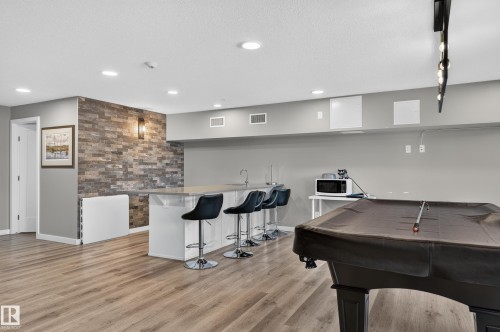 Wood-finish flooring, accent wall with sconce lighting, built-in wet bar with seating, recessed ceiling lighting, and track lighting fixture - #131 5504 Schonsee Dr Nw, Edmonton, AB - Indoor Photo Showing Other Room