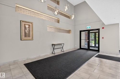 Lobby entrance featuring double glass doors, tile flooring, and decorative wall cutouts with integrated lighting - #131 5504 Schonsee Dr Nw, Edmonton, AB - Indoor Photo Showing Other Room
