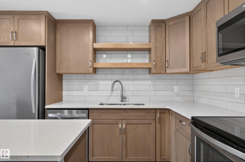 Wood-finish cabinetry, light-toned countertops, white subway tile backsplash, stainless steel appliances, and an undermount sink - #131 5504 Schonsee Dr Nw, Edmonton, AB - Indoor Photo Showing Kitchen With Stainless Steel Kitchen With Double Sink
