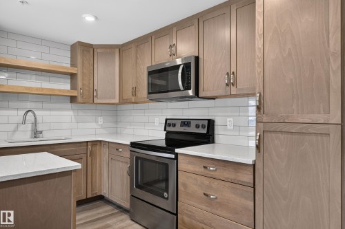 Stainless steel appliances, wood-finish cabinetry, white subway tile backsplash, light-toned countertops, and an undermount sink - #131 5504 Schonsee Dr Nw, Edmonton, AB - Indoor Photo Showing Kitchen With Upgraded Kitchen