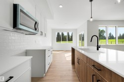 Bright kitchen featuring white cabinetry, a built-in microwave, white subway tile backsplash, a large island with white countertops, and wood-finish flooring - 