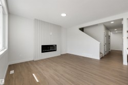 Spacious room with wood-finish flooring, a contemporary fireplace feature wall, recessed lighting, and a prominent window - 