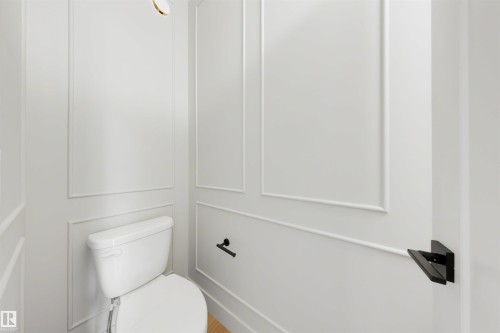 White paneled walls with decorative molding, a white toilet, and matte black hardware - 16 Grayson Green, Stony Plain, AB - Indoor Photo Showing Bathroom