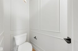 White paneled walls with decorative molding, a white toilet, and matte black hardware - 