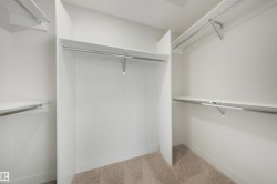 Closet featuring white built-in shelving, chrome hanging rods, and light-colored carpet flooring - 