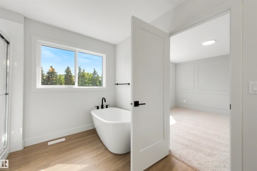 Freestanding bathtub with matte black fixtures, wood-finish flooring, and bright window - 16 Grayson Green, Stony Plain, AB - Indoor Photo Showing Other Room