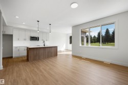 Open-concept living space featuring wood-finish flooring, a kitchen island with a wood-finish base, white cabinetry, and large windows - 