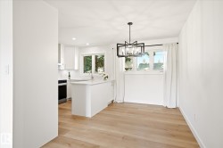 Open-concept kitchen and dining area featuring light wood-finish flooring, a contemporary black geometric chandelier, white cabinetry, a kitchen island, and multiple windows - 