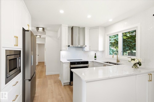 Modern kitchen featuring white cabinetry with gold-tone hardware, stainless steel appliances including a built-in microwave and refrigerator, and a U-shaped countertop - 4708 104A Avenue Nw, Edmonton, AB - Indoor Photo Showing Kitchen With Double Sink With Upgraded Kitchen