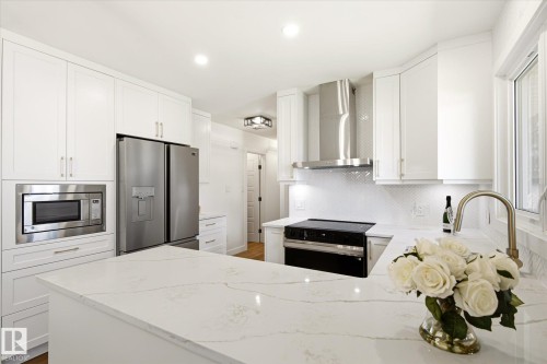 Contemporary kitchen featuring white cabinetry, a large center island with a stone countertop, stainless steel appliances, a tile backsplash, and recessed lighting - 4708 104A Avenue Nw, Edmonton, AB - Indoor Photo Showing Kitchen