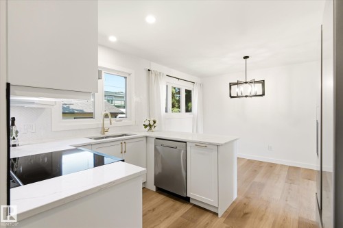 Modern kitchen and dining area featuring white cabinetry, light-colored countertops, a built-in cooktop, and stainless steel appliances - 4708 104A Avenue Nw, Edmonton, AB - Indoor Photo Showing Kitchen With Double Sink